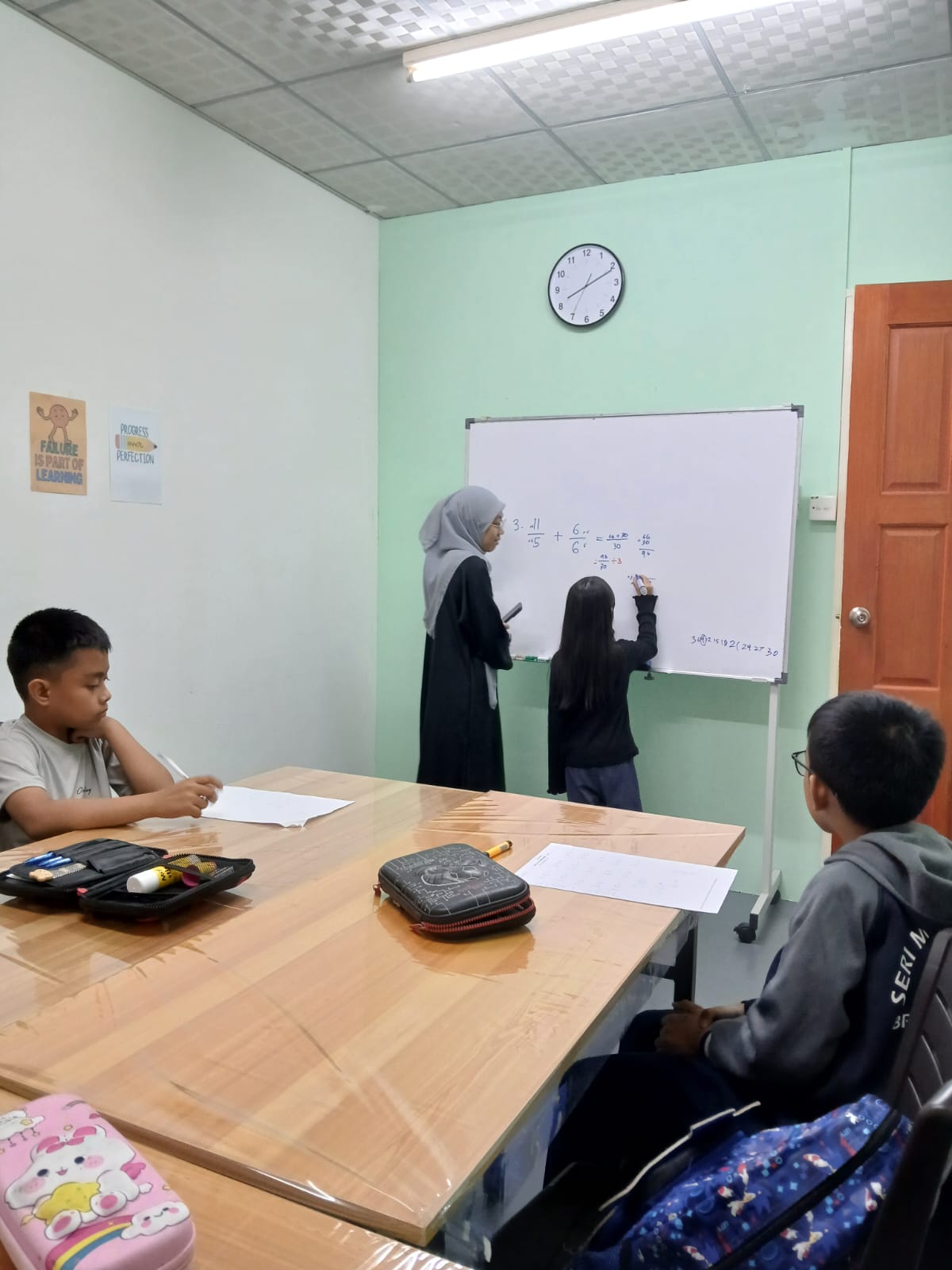 An AFTC tutor supporting a student at the whiteboard during a maths lesson
